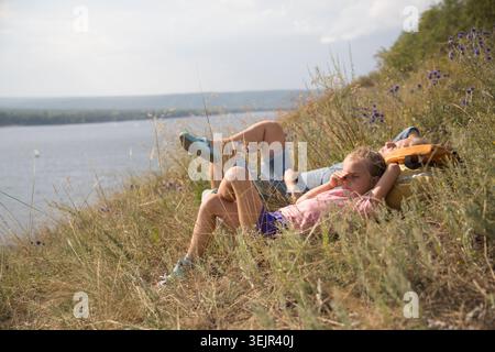 Glückliche Familienmutter und Tochter, die auf dem Gras am Berghang liegen und in die Ferne schauen Stockfoto