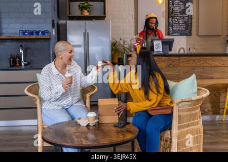 Verschiedene Freundinnen sitzen am Café-Tisch und teilen sich Kaffee und Dessert, eine trägt Senfpullover. Duo, gemütlich, warm, rustikal, Stockfoto