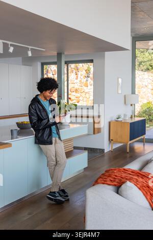 Afroamerikaner lehnt sich auf pastellblaue Insel mit Smartphone und Zitronen, Kopierraum. Modern, minimalistisch, offen, Natur Stockfoto