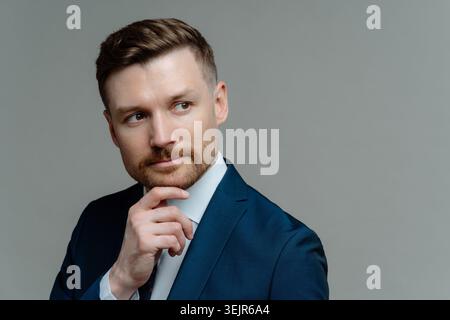Ein durchdachter bärtiger Geschäftsmann hält das Kinn und denkt, dass etwas wegschaut, macht die Entscheidung in formeller Kleidung sieht nach vorne Stockfoto