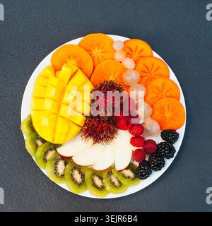 Scheiben reifer exotischer Früchte auf weißem Teller. Kiwi, Mango, Himbeere, Heidelbeere und Persimmon. Obstsortiment. Draufsicht. Heiz Stockfoto
