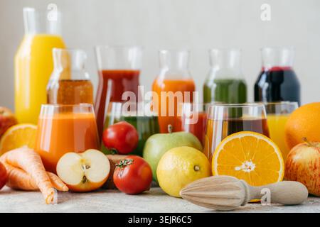 Horizontaler Schuss von frischem Obst und Gemüse auf weißem Tisch, Gläser mit Saft und Orangenpresse. Gesundes Getränkekonzept. O Stockfoto