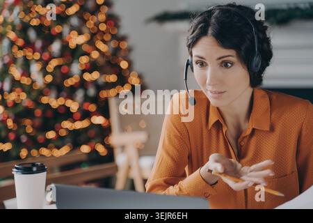 Junge Geschäftsfrau im Headset, die während eines Online-Meetings zu weihnachten im Büro mit Kollegen spricht Stockfoto