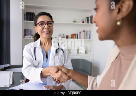 Fröhlicher Arzt mittleren Alters beim Händeschütteln mit jungen schwarzen Patienten Stockfoto