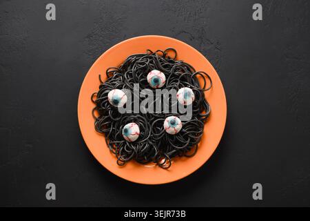 Halloween lustige italienische schwarze Pasta Tintenfisch Tinte verziert Horror Augen in orange Platte mit Rauchtrank auf schwarzem Hintergrund. Horror-Essen für Party. Anzeigen Stockfoto