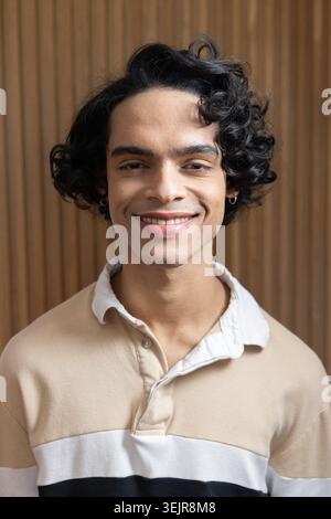 Teenager-Indianer lächelnd mit beigefarbenem weißem Hemd und Creolen in Holzlattenwand des Studios. Porträt, Nahaufnahme, Kopfaufnahme, Stockfoto