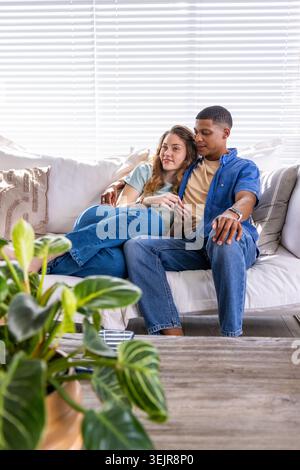 Diverse Paare sitzen dicht auf hellem Sofa in hellem Wohnzimmer neben hölzernem Couchtisch. Couch, Romantik, entspannt, Tageslicht Stockfoto