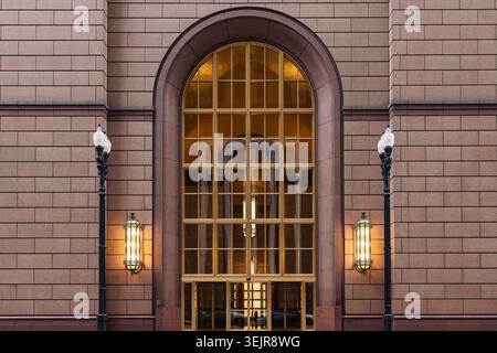 Ein großes Fenster mit Gitterdesign befindet sich in einem historischen Gebäude in Chicago. Straßenlaternen beleuchten den Eingangsbereich am Abend. Die Architektur Stockfoto