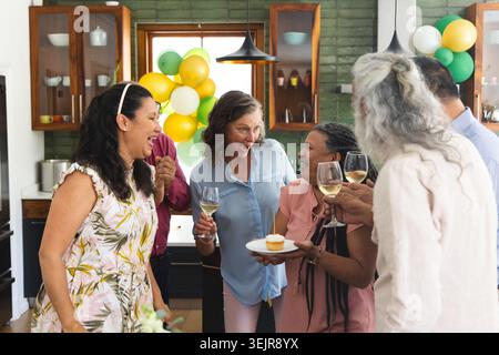 Verschiedene Freunde und Familie lachen und halten Weingläser in der Nähe von Ballons in der Küche. Mehrgenerationen, Feier, gath Stockfoto