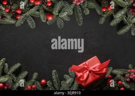 Weihnachtsrahmen mit rotem Geschenk und Deko auf Schwarz. Weihnachtsgrußkarte. Stockfoto