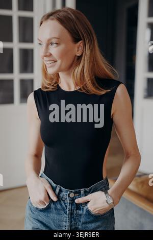 Lächelnde Frau in schwarzem ärmellosem Top, die zuhause drinnen steht Stockfoto