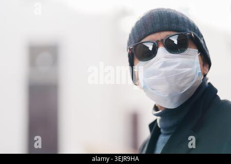 Mann mit Schutzmaske und Sonnenbrille draußen auf der Winterstraße Stockfoto