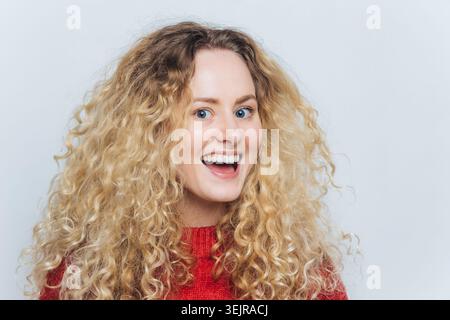 Glückliche blonde Frau lächelt im Studio-Porträt mit lockigen Haaren Stockfoto