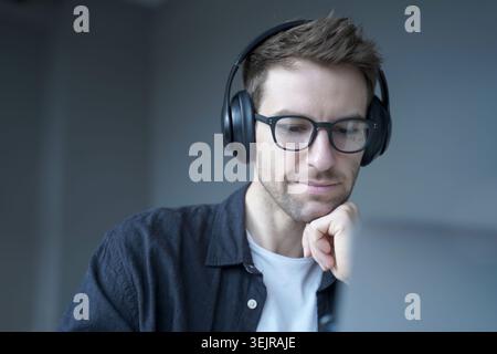 Ein fokussierter Mann, der Kopfhörer trägt und während eines Online-Meetings zu Hause am Laptop arbeitet Stockfoto