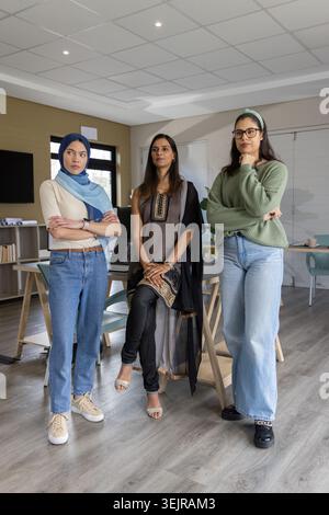 Verschiedene weibliche Kollegen stehen im Besprechungsraum, tragen Hijab und Tunika und halten einen Laptop. Büro, Arbeitsplatz, Zusammenarbeit, Tee Stockfoto