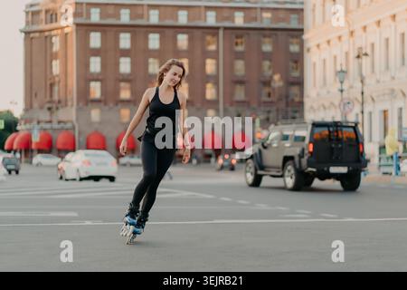 Junge Frau Roller Skating auf der City Street mit schwarzer Sportswear im urbanen Verkehrshintergrund Stockfoto