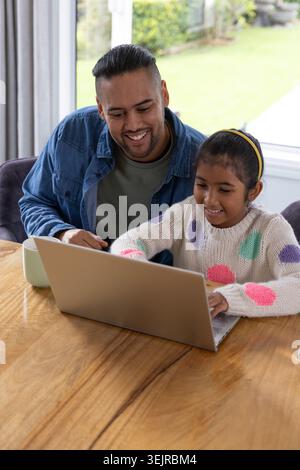 Asiatischer Mann lehnt sich an und Kind Mädchen tippt auf silbernem Laptop am Tisch mit Polka Dot Pullover. Tochter, Elternteil, Haus, Natur, Pädagoge Stockfoto