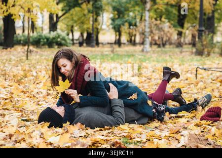 Das junge Paar, das im Herbst liegt, verlässt den Park und genießt gemeinsam einen romantischen Outdoor-Moment Stockfoto