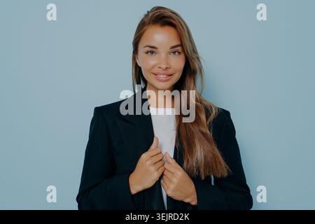 Professionelles Geschäftsporträt der jungen Frau in schwarzem Blazer auf sauberem blauem Studio-Hintergrund Stockfoto