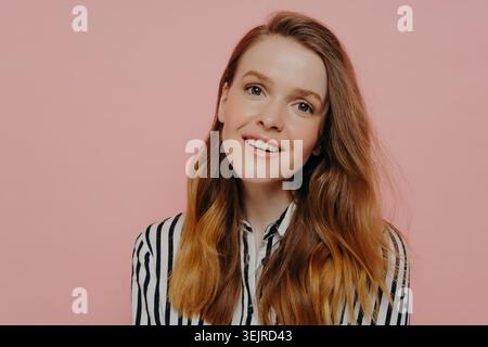 Junge Rothaarige lächelnde Frau im Studio Beauty Porträt auf rosa Hintergrund mit gestreiftem Hemd Stockfoto