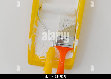 Malerwalze und Pinsel in gelbem Fach Nahaufnahme mit weißer Farbe für Heimwerkerrenovierung und Inneneinrichtung Stockfoto