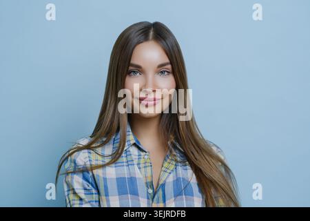 Smiling Young Woman Studio Porträt auf blauem Hintergrund trägt lässiges kariertes Hemd mit sauberem Kopierraum und selbstbewusstem Ausdruck Stockfoto