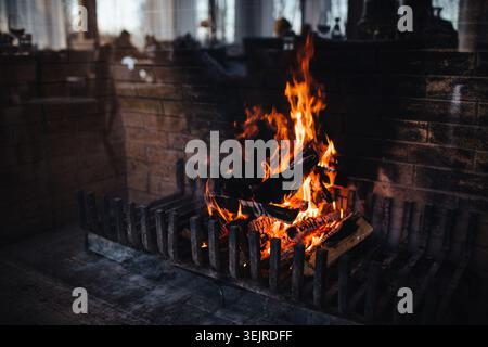Warmer Kamin brennende Holzfässer in Ziegelsteinhund Nahaufnahme gemütliches Indoor-Feuer mit orangefarbenen Flammen und dunklem Hintergrund Stockfoto