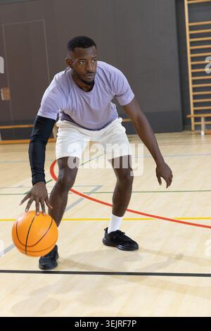 Mittelgroßer Afroamerikaner, der Basketball auf dem Platz tröpfelt, lila Hemd, schwarzer Ärmel. Fitnessraum, Hartholz, Leinen, La Stockfoto