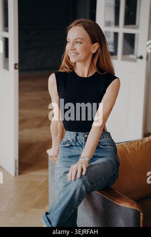Junge rothaarige Frau sitzt auf einem Ledersessel im modernen Innenraum Stockfoto
