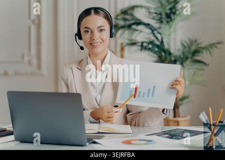 Geschäftsfrau, die ein Headset trägt, präsentiert Wachstumsdiagramm bei der Arbeit mit einem Notebook im Büro Stockfoto