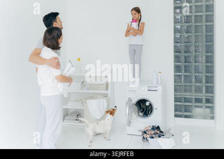 Eltern beobachten die Tochter, die mit Hund auf der Waschmaschine steht Stockfoto