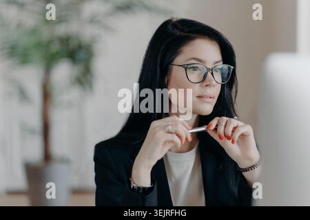 Die junge Geschäftsfrau mit Brille arbeitet nachdenklich am Computer in modernen Büros Stockfoto