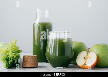 Grüner Gemüsesaft im Glas und Flasche mit Äpfeln und Sellerie auf dem Tisch Stockfoto