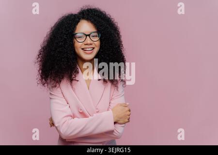 Eine junge Berufsfrau mit Brille und rosa Blazer posiert im Studio Stockfoto