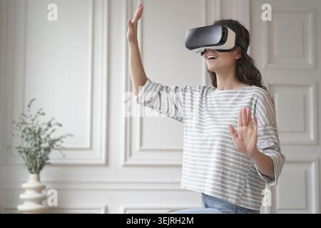 Die junge Frau verwendet Virtual-Reality-Headset und Gesten in hellen, modernen Räumen Stockfoto