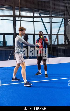 Verschiedene männliche Freunde in Sportbekleidung üben Padel auf dem blauen Platz mit Schlägern und Bällen. Sportlich, Teamwork, modern, Urban, per Stockfoto