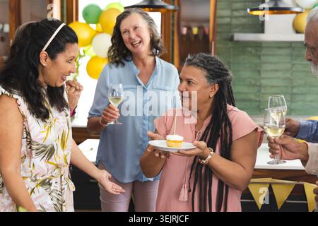 Weibliche Freunde mit einem älteren Mann, der an der Küchenzeile feiert und einen Cupcake mit brennender Kerze hält. Feiern, feiern, Treffen Stockfoto