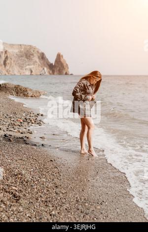 Frau Strandshirt steht an einem felsigen Ufer in einem karierten Hemd und genießt die Meereswellen und die Küstenlandschaft Stockfoto