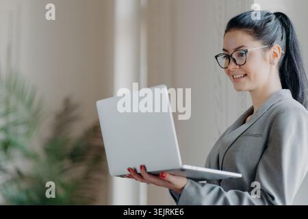 Geschäftsfrau, die in einem hellen, modernen Büro einen Laptop hält Stockfoto