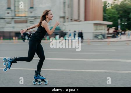 Junge Frau Rollerblades auf der Stadtstraße in schwarzer Sportbekleidung und blauen Inline-Skates Stockfoto