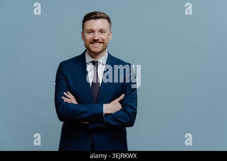 Ein selbstbewusster, bärtiger Unternehmer hält die Arme überkreuzt ein Lächeln und ist gerne in formeller Kleidung gekleidet Stockfoto