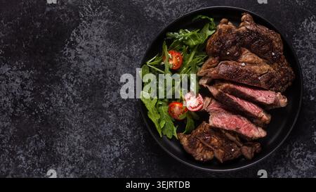 Gegrilltes Rindersteak mit Gewürzen auf schwarzem Teller, Draufsicht. Stockfoto