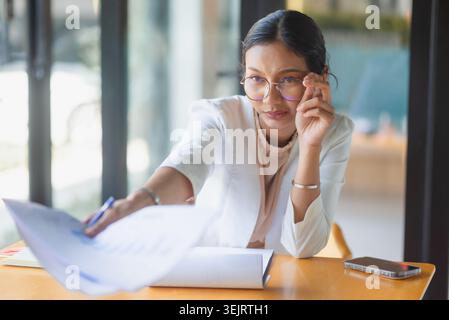 Seriöse Geschäftsfrau, die mit Dokumenten und Stift über den Bürotisch greift, Berichtsdetails überprüft, Daten diskutiert, Geschäftsentscheidungen getroffen, Probleme gelöst Stockfoto