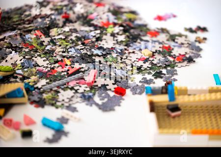 Ein unsortierter Stapel von Puzzleteilen aus Pappe liegt auf einer weißen Fläche neben mehreren Plastikspielzeugbauziegeln und Elementen unter b verstreut Stockfoto