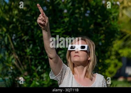 Eine Frau trägt eine Brille, um eine Sonnenfinsternis zu beobachten und zeigt mit dem Zeigefinger auf die Sonne Stockfoto