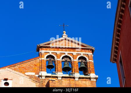 Der Glockengiebel der Kirche Santa Maria del Giglio erhebt sich in Venedig in den blauen Himmel. Drei historische Bronzeglocken hängen in bogenförmigen Ziegelöffnungen Stockfoto