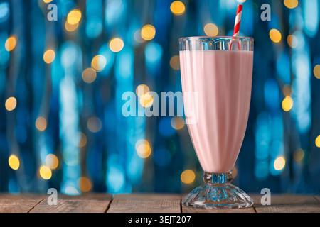 Erdbeermilchshake in hohem Glas mit gestreiftem Stroh auf rustikalem Holztisch Stockfoto
