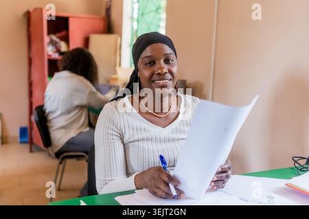 Porträt einer lächelnden jungen afrikanischen Geschäftsfrau, die am Schreibtisch im Büro sitzt und an einem Laptop arbeitet, Unternehmertum in afrika Stockfoto