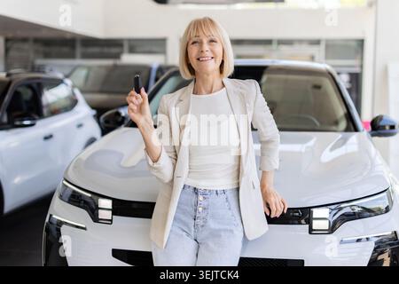 Eine ältere Frau, die den Autoschlüssel hält, während sie vor dem neuen Fahrzeug posiert Stockfoto