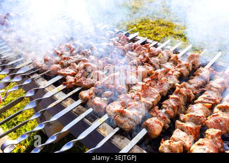 Die Leute versammeln sich am Grill, während sie Fleisch auf Spießen kochen und das warme Sommerwetter draußen im Garten genießen. Stockfoto